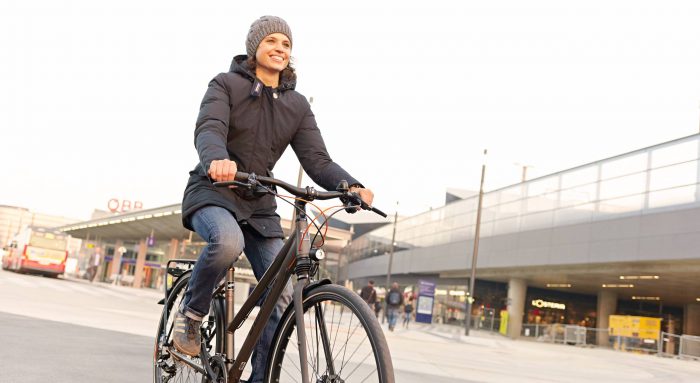 Junge Frau fährt auf ihrem Fahrrad, begleitet mit Winterjacke und Haube, am Hauptbahnhof vorbei. Foto von Stephan Doleschal.