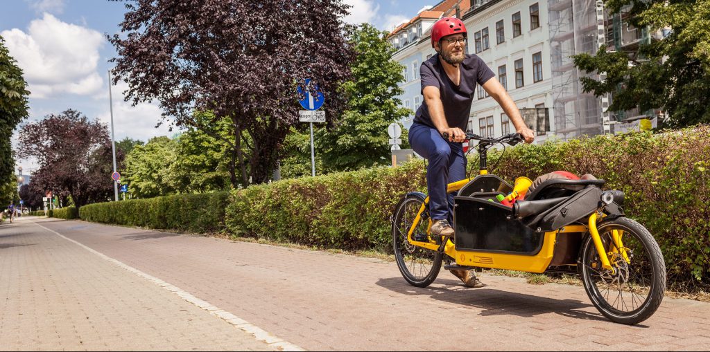 Ein Mann fährt mit einem gelben Transportfahrrad auf einem Radweg