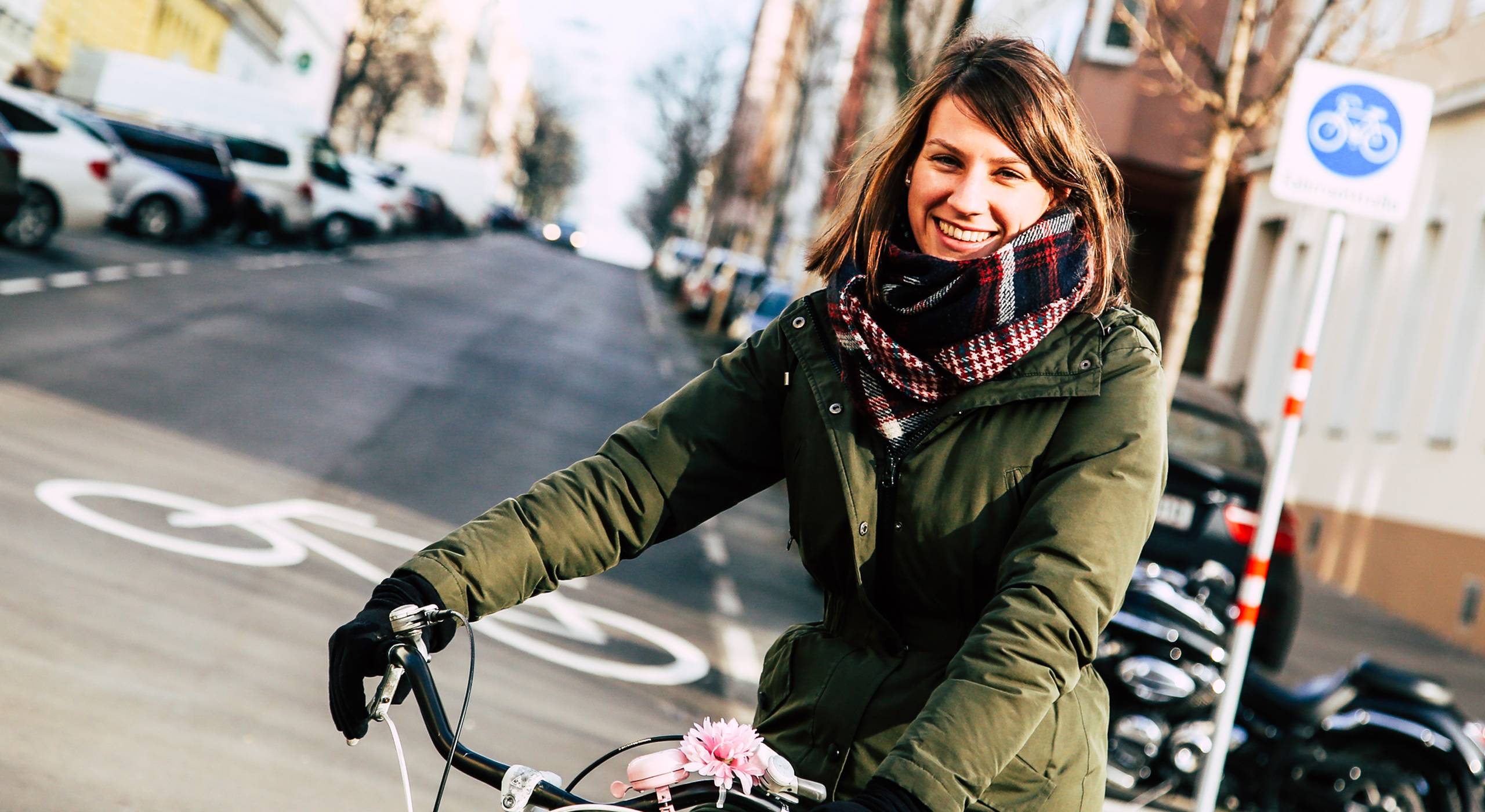 Junge Frau auf dem Fahrrad lächelt in die Kamera. Im Hintergrund sieht man das Schild und das Bodenpiktogramm, die die Fahrradstraße Goldschlagstraße als solche kennzeichnen. Foto: Christian Fürthner