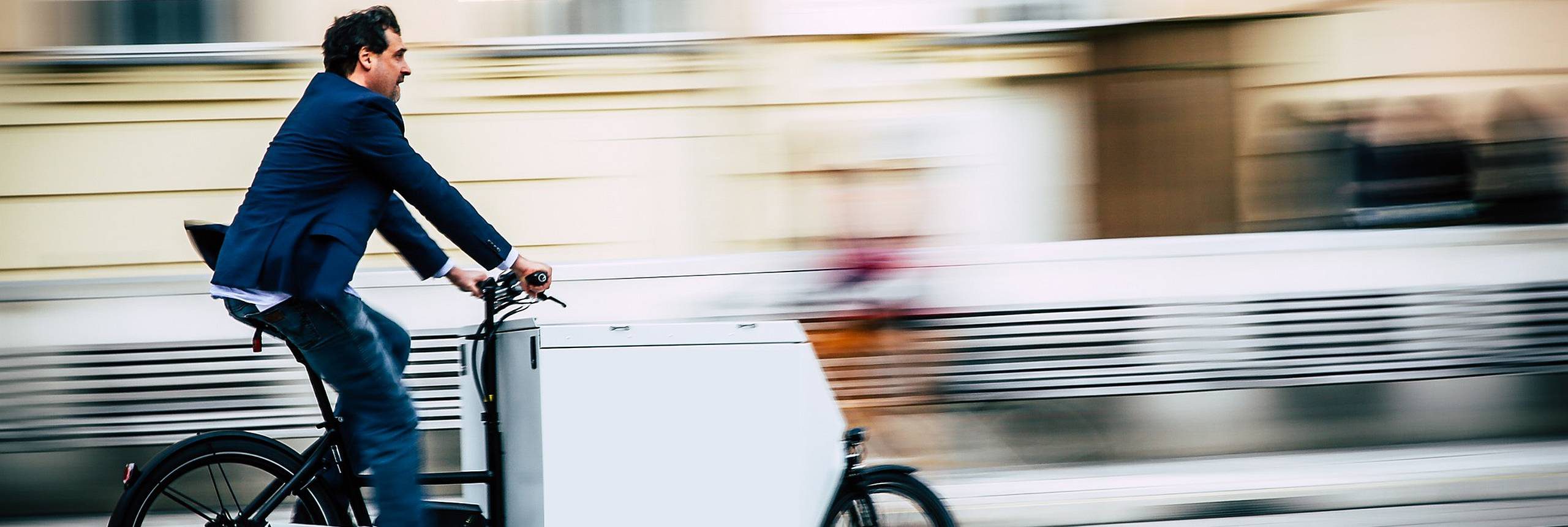 Mann fährt ein Transportfahrrad. Er trägt ein blaues Sakko. Foto: Christian Fürthner