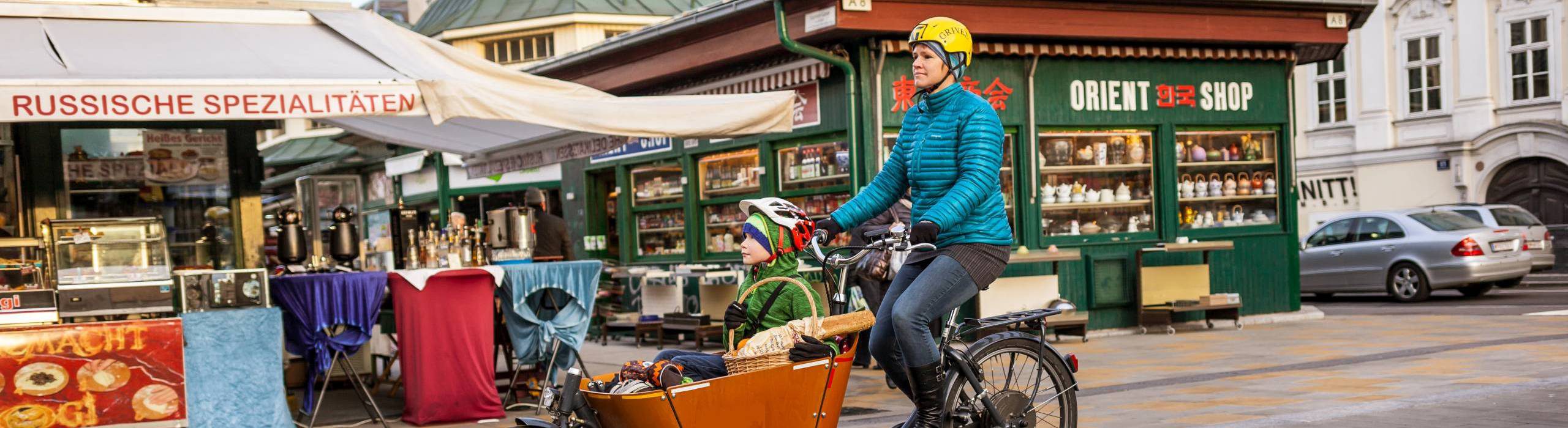 Frau fährt ein Transportfahrrad. Im Korb sitzt ihr Sohn. Foto: Stephan Doleschal