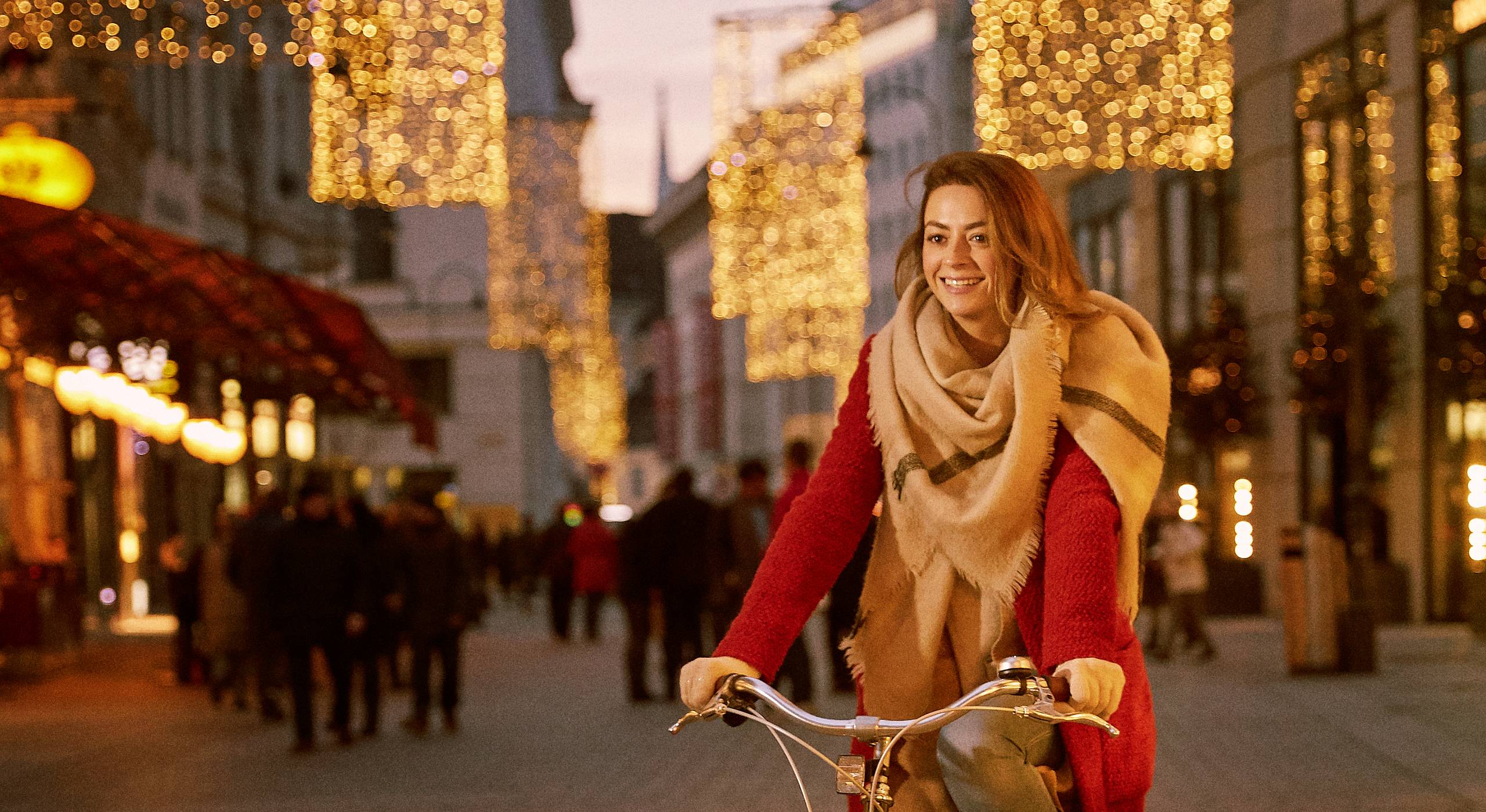 Frau in rotem Mantel fährt mit dem Fahrrad am festlich beleuchteten Kohlmarkt in der Winer Innenstadt. Foto von Philipp Schönauer