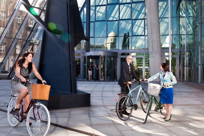 Zwei Frauen und ein Mann auf Fahrrädern vor dem Eingang eines großen Bankgebäudes.