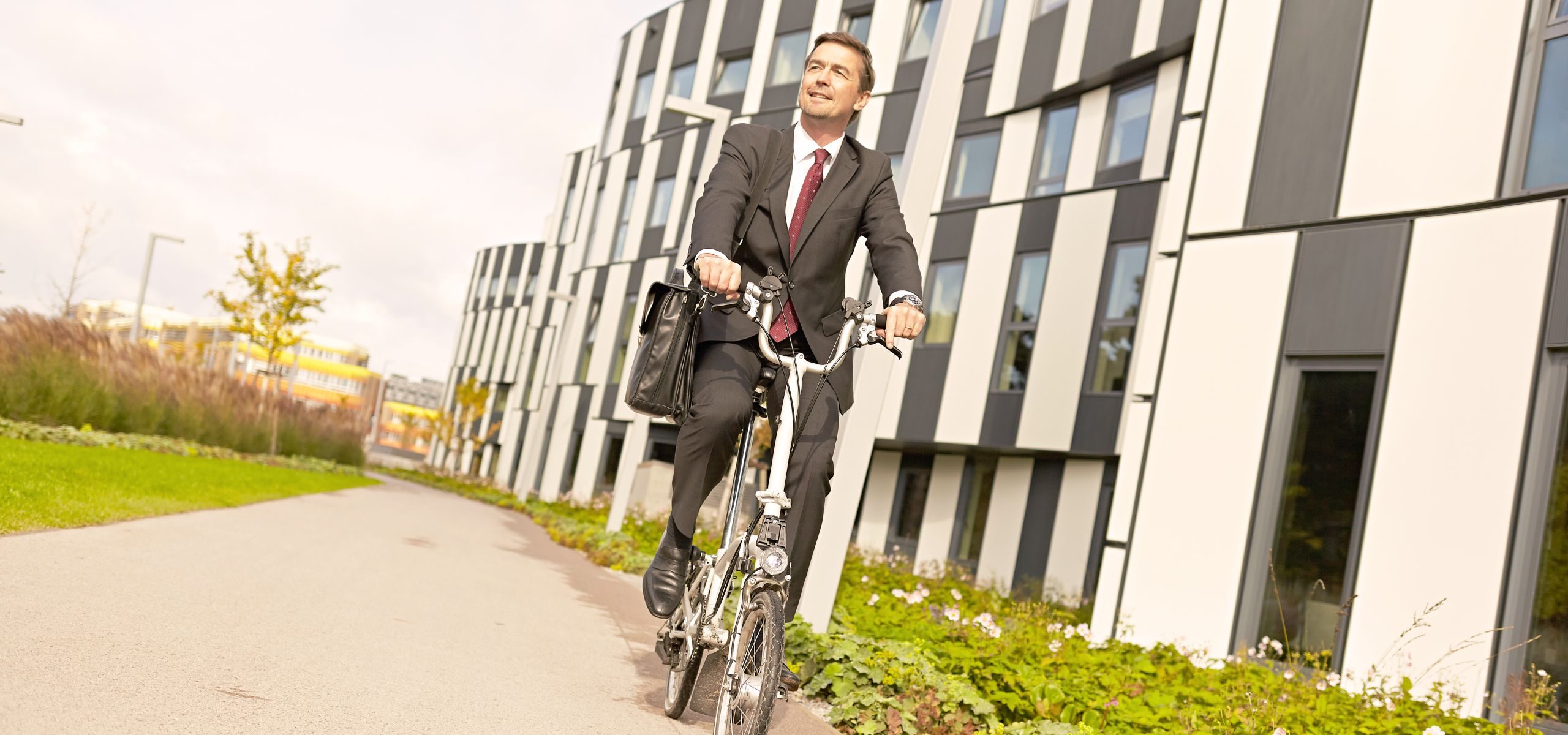 Mann fährt auf seinem Klapprad an einem modernen Gebäude am WU Caampus vorbei.