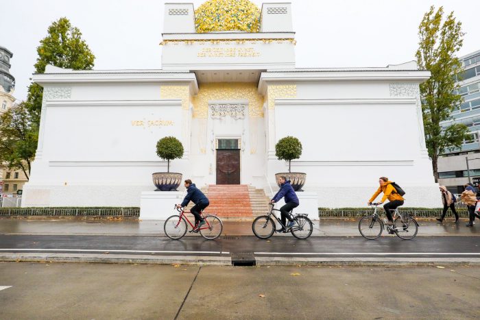 Drei Radler fahren am neuen Radweg enmtlang der Linken Wienzeile an der Secession vorbei.