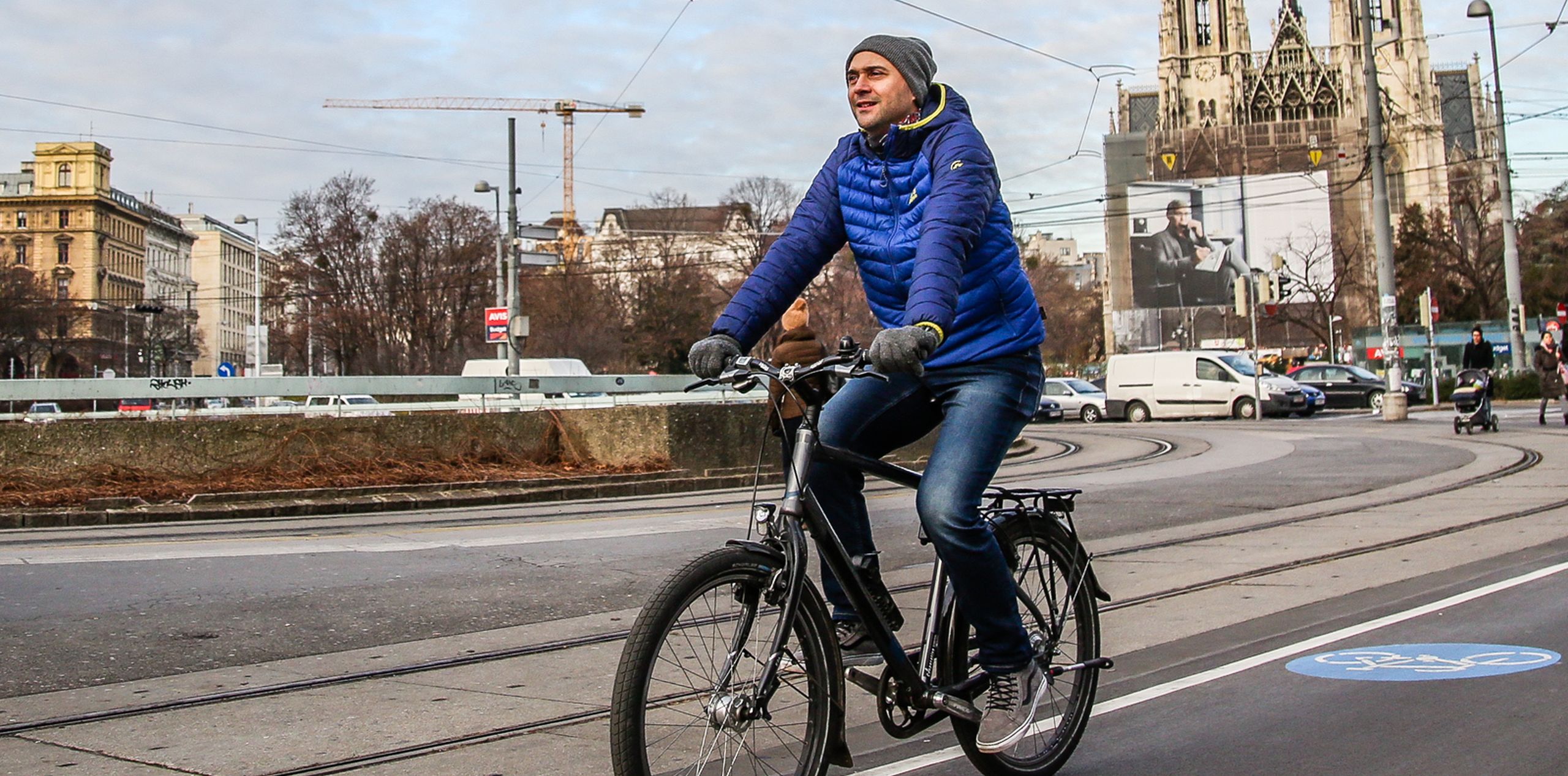 Radfahrer radelt entlang des Radwegs am Schottenring. Im Hintergrund sieht man die Votivkirche.