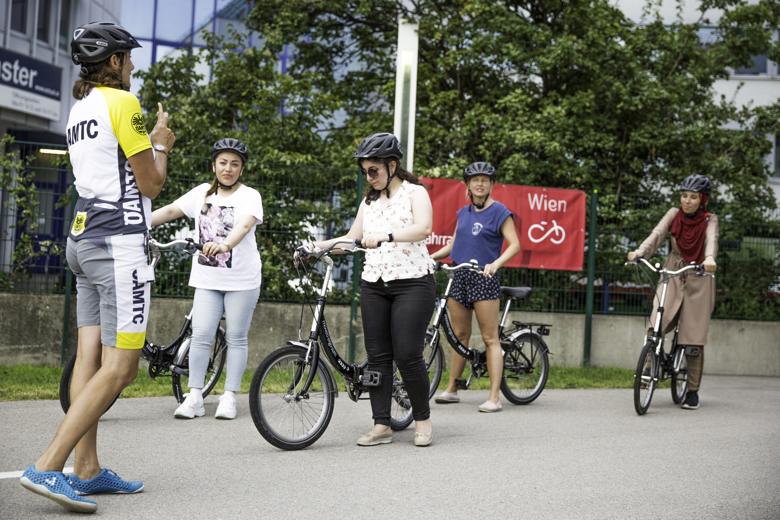 Mehrere Frauen stehen mit ihren Fahrrädern auf dem Übungsplatz. Radlehrerin Daniela steht vor ihnen und erklärt etwas