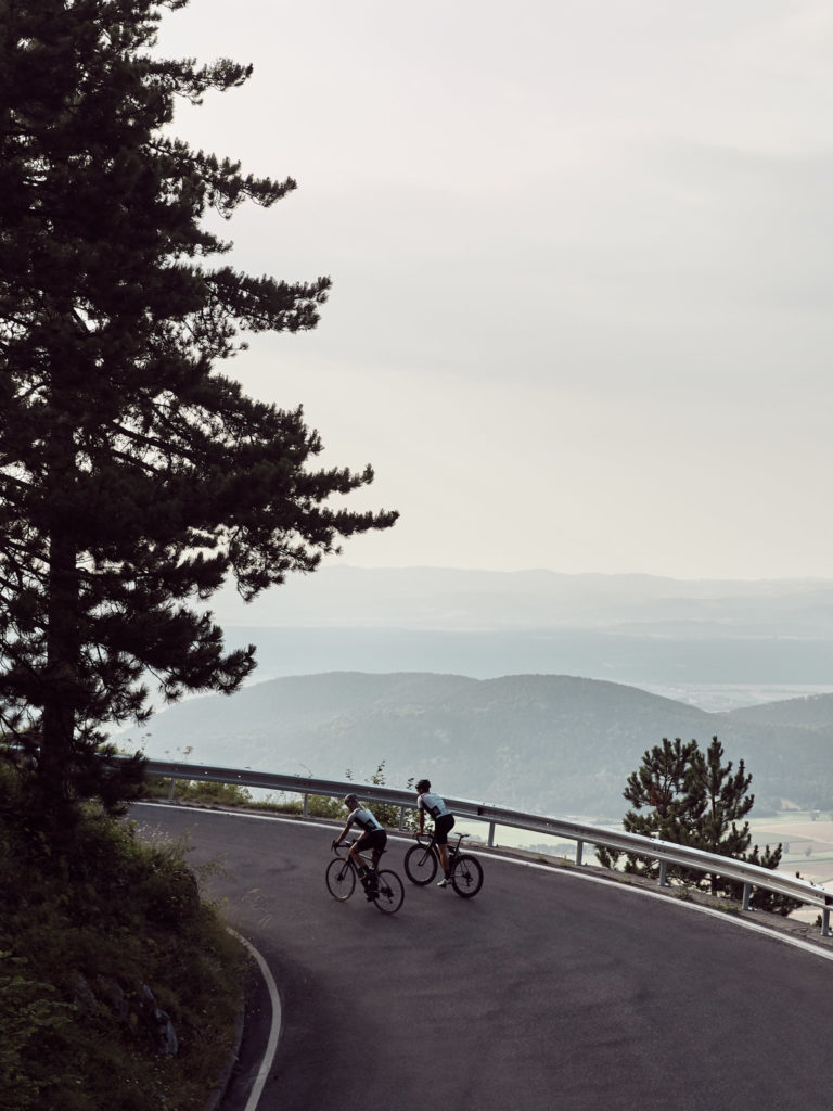 Nora und eine anderer Rennradfahrer fahren auf einer Bergstraße um die Kurve, im Hintergrund hügelige Landschaft