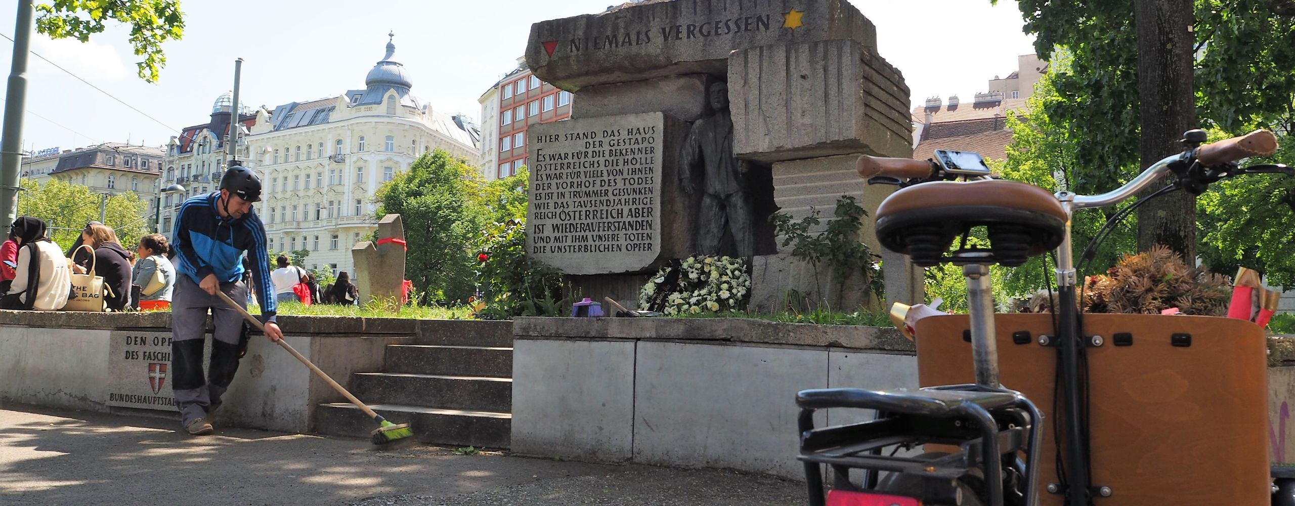 Am Morzinplatz: Martin macht das Denkmal besenrein und kehrt. Im Vordergrund steht das Transportfahrrad.